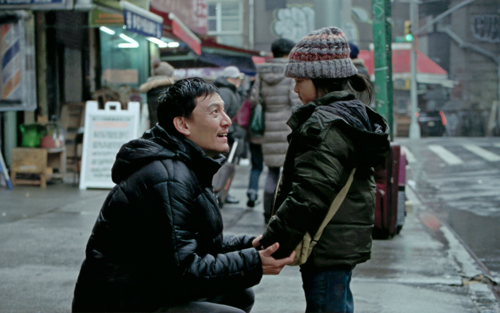 Chang Chen dans le rôle de Lu, agenouillé dans une rue de New York, tenant les mains de sa fille Yaya jouée par Carabelle Manna Wei, scène du film Les Lumières de New York