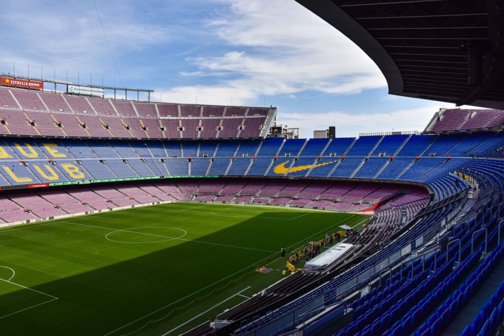 Wide view of the iconic Camp Nou stadium in Barcelona, showcasing its vast empty stands and lush green field.