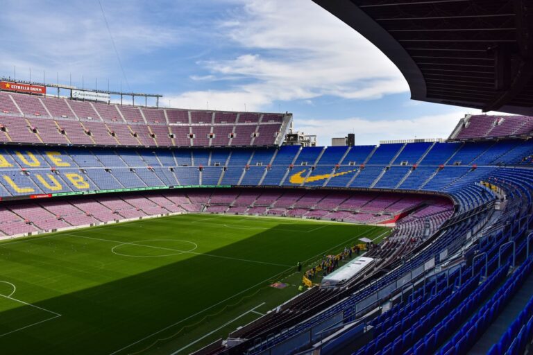 Wide view of the iconic Camp Nou stadium in Barcelona, showcasing its vast empty stands and lush green field.