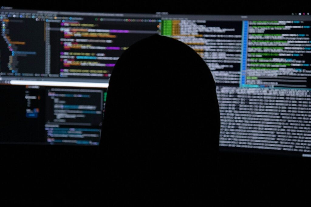 A person in silhouette against multiple computer monitors displaying lines of code