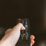Close-up of a hand using a remote control to operate a TV, emphasizing modern technology.