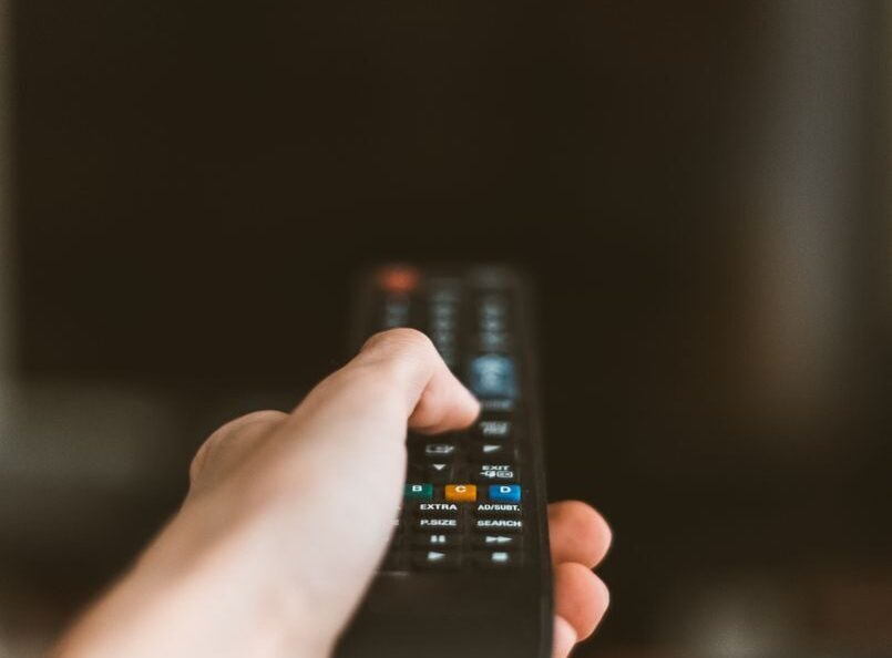 Close-up of a hand using a remote control to operate a TV, emphasizing modern technology.